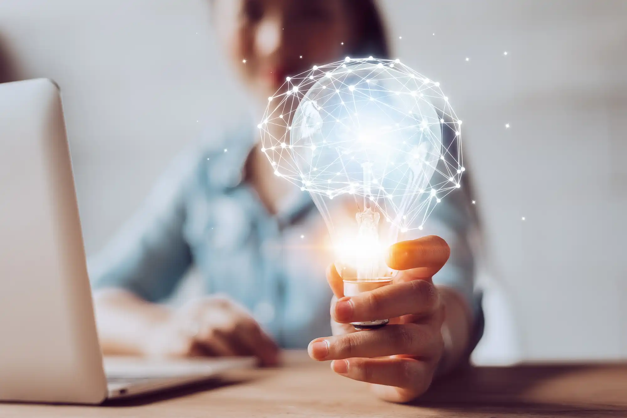 Person holding a glowing lightbulb with a digital brain network above it, symbolizing innovation and artificial intelligence.
